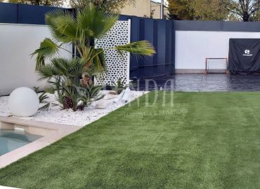 Jardín con piscina, pradera verde y vegetación ornamental