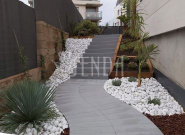 Diseño de jardín en desnivel con escaleras, grava blanca y vegetación ornamental
