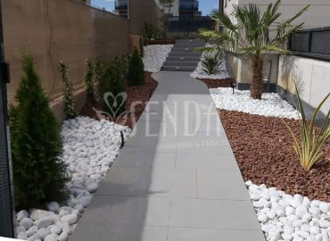 Diseño paisajístico en pasillo lateral con grava blanca, palmeras y recorrido integrado